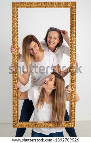 Family composed by mother and two twin sisters pose inside a pictorial frame in a photographic studio and in a very funny attitude.