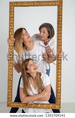 Family composed by mother and two twin sisters pose inside a pictorial frame in a photographic studio and in a very funny attitude.