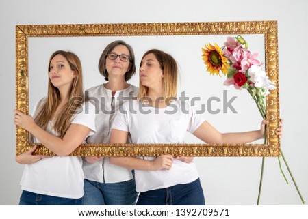 Family composed by mother and two twin sisters pose inside a pictorial frame in a photographic studio and in a very funny attitude.