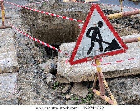 Replacement of heating pipes. Repair of pipes with drinking water. The texture of excavated earth. Metal pipe under the ground. Road sign indicating repair work.