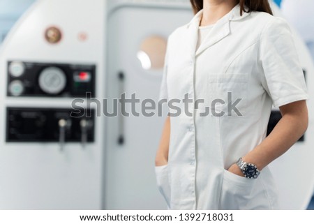 Unrecognizable doctor holding hands in pockets while standing in front of hyperbaric chamber at clinic. 