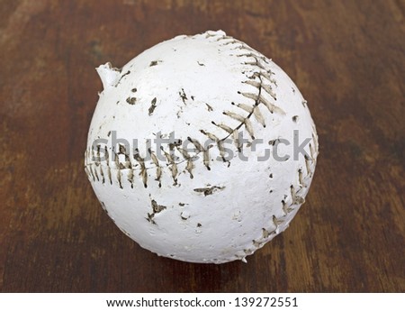 A softball that has been chewed and bitten by a dog on a wood background.