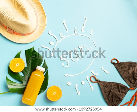 Summer beach accessories sunscreen hat bathing bottle orange juice blue background text SUN. The concept relaxation