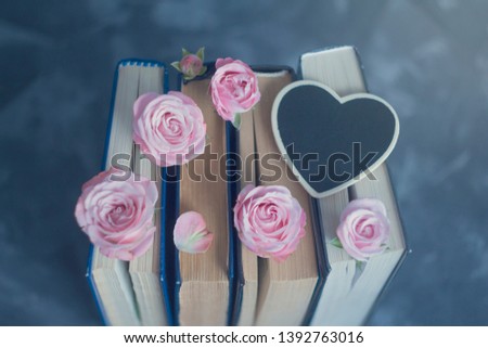 Pile of the old books and pink roses white black chalk board heart on the concrete surface