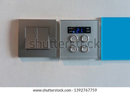 Grey metallic light switch and air condition controller with digital display against white wall background.