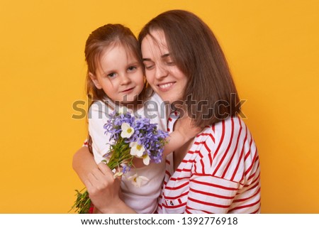 Photo of happy mother and kid. Affectionate female holds on tight her little charming daughter. Cute child gives bouguet of flowers to her mummy, congratulates with Mother's Day! Happyness concept.
