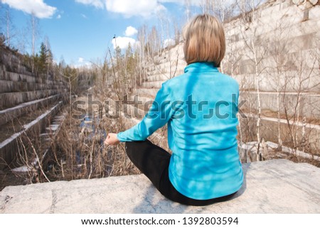 Portrait of a meditating blonde outdoors on the background of a marble quarry. Unity with the concept of nature. Girl meditates in the windbreaker, his hands in the wise om.