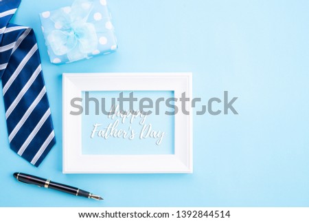 Happy fathers day concept. Top view of blue tie, beautiful gift box, coffee mug, white picture frame with happy father's day text  on bright blue pastel background.