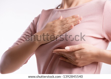 Woman hand checking lumps on her breast for signs of breast cancer on gray background. Healthcare concept.