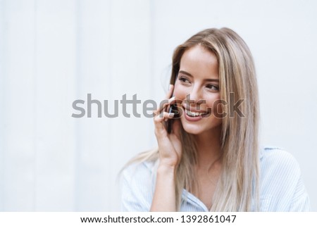Portrait of a smiling blonde woman talking on mobile phone, standing outdoors