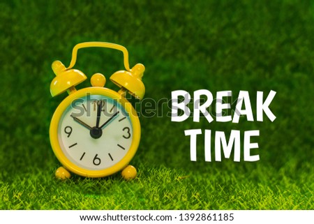 yellow alarm clock on a background of green grass with the words Break time