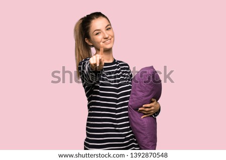 Pretty woman in pajamas showing and lifting a finger on isolated pink background