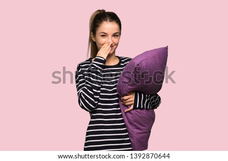 Pretty woman in pajamas smiling a lot while covering mouth on isolated pink background