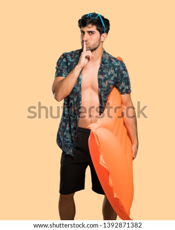 Man in trunks showing a sign of silence gesture putting finger in mouth over isolated yellow background