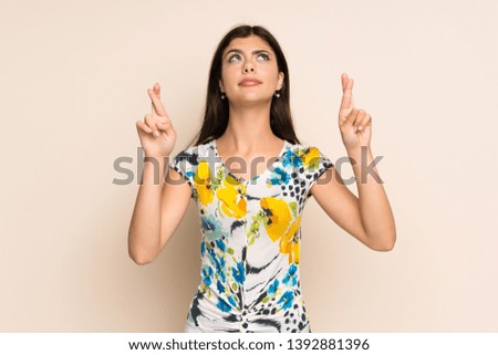 Teenager girl with floral dress with fingers crossing and wishing the best