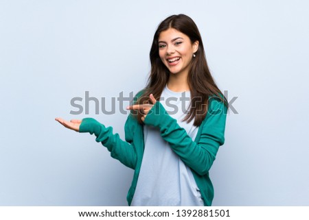 Teenager girl over blue wall holding copyspace imaginary on the palm to insert an ad