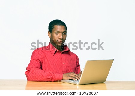Teen boy types on a laptop computer as he sits at a desk and looks serious. Horizontally framed photograph
