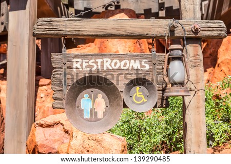 wooden and round metal sign of the restrooms decorated with old lamp