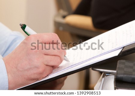 Close-up shot of a man taking notes at a business meeting, seminar or conference