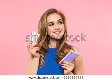 Image of a beautiful happy young pretty woman posing isolated over pink wall background holding credit card using mobile phone.