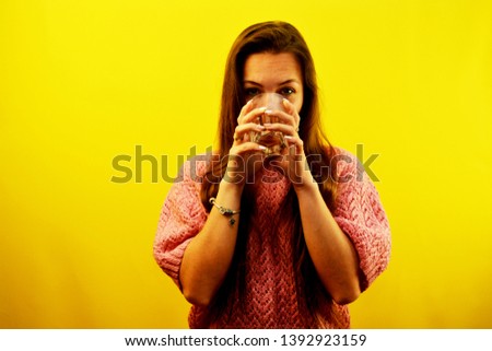 young beautiful brunette girl in a yellow sweater on a yellow background with a glass of water in her hands