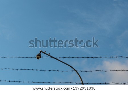 Two birds are perched on a cctv which is bordered by barbed wire against a background of bright blue sky