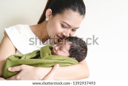 Loving mother with her newborn baby on her arms.Beautiful Asian mom holding newborn baby in arms and kiss in the bedroom.