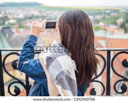 Young asian woman taking photos with her smartphone on the rooftop. View of Kromeriz, Czech Republic.