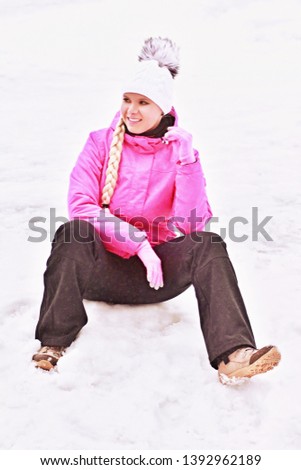 Beautiful European skier woman with long blond pigtail and white knitted hat dressed pink sporty clothes sitting in the ski resort on background. Leisure activities and winter sports concept.