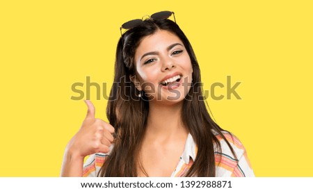 Teenager girl on summer vacation giving a thumbs up gesture over isolated yellow background