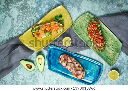 Bruscheta with different fillings on blue, green and yellow plates. Beautiful serving dishes. Light gray background. Restaurant menu