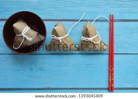 Row of Zongzi or rice dumpling on Dragon Boat Festival, Asian traditional food, one pieces in wooden bowl and two pieces on blue wooden plank with chopstick, isolated, free space, top view, flat lay