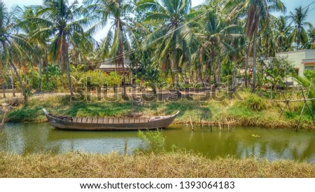 Vietnam: Beautiful scenery in the Mekong-Delta. Wooden boat in a small river in front of palm trees and a house.