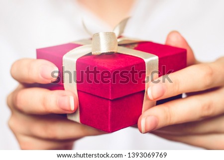 Female hands holding a small red box with a gift. Birthday concept
