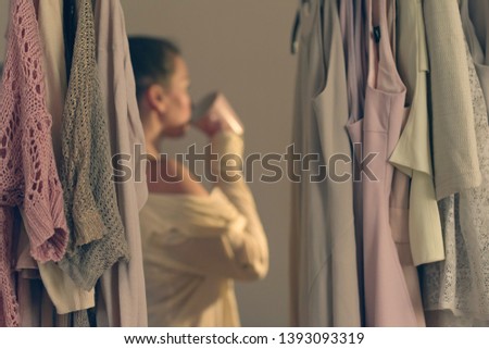 Unfocused young woman with cup of coffee and standing in front of her wardrobe early morning. View from inside the wardrobe