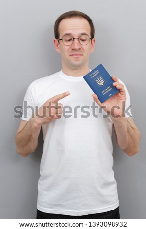 European man with a Ukrainian passport in his hands, wearing glasses, wearing a white T-shirt, a citizen of the country with a passport, studio photo with a man