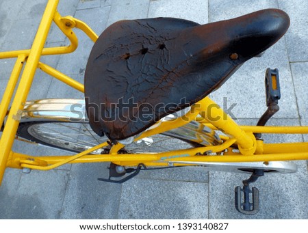 old yellow bicycle close-up with dried out leather seat and carrier frame and pedals on gray stone paving. abstract view seen from above. vintage and retro style bicycle. 