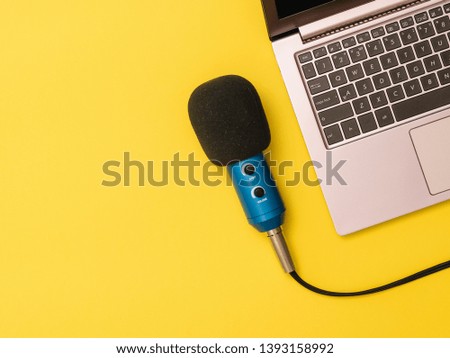 Blue microphone and a laptop at the yellow table. The concept of workplace organization.