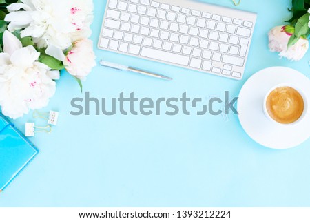 Flat lay top view home office workspace background with white modern keyboard, coffee and peony flowers, copy space on blue background
