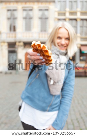 Young beautiful woman in a blue jacket holding a traditional Belgian waffle on the background of the Great Market Square in Brussels, Belgium. The main tourist attraction of the city. The central
