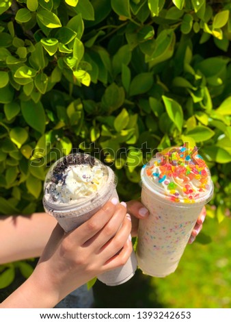 Milk shakes on a sunny day. Fruity pebble on milkshake with a green background on a summer day. A young girl with nice nails holding milkshakes. Delicious food.