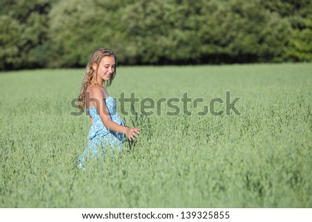 Beautiful teenager girl walking happy across a green oat meadow touching the herbs