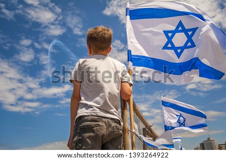 Israeli kid watching the aviation show on the 71 Israel Independence Day with a flag of Israel against the blue sky. Royalty-Free Stock Photo #1393264922