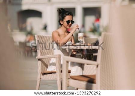 portrait of beautiful woman in sunglasses and dress sitting in a cafe and drinking coffee on a sunny summer day.