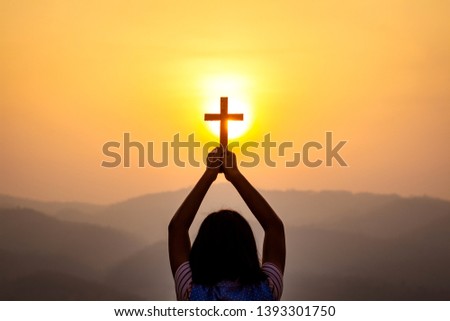human praying to the GOD while holding a crucifix symbol with bright sunbeam on the sky