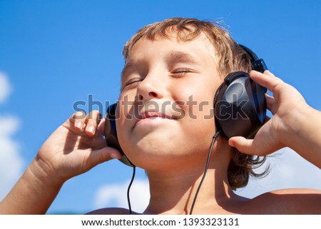 Boy listens to music on headphones on background of blue sky