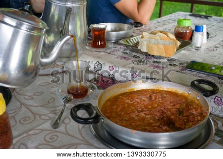 Pouring tea from tea pot to glass. Breakfast preparation concept. Traditional Turkish brewed tea drink in morning also as known "Cay" or "Turk Cayi". Menemen and bread with Turkish Tea. 