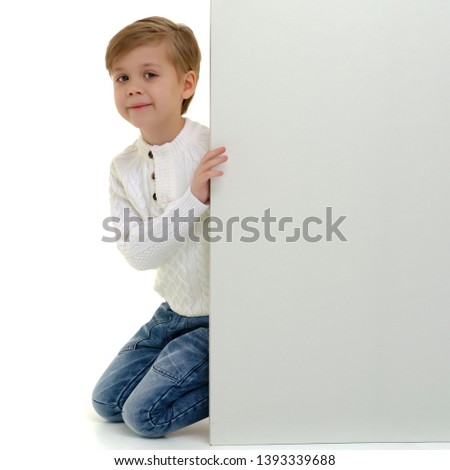 A little boy looks through an empty banner on which you can write any text. The concept of a happy childhood and advertising of children's goods. Isolated on white background.