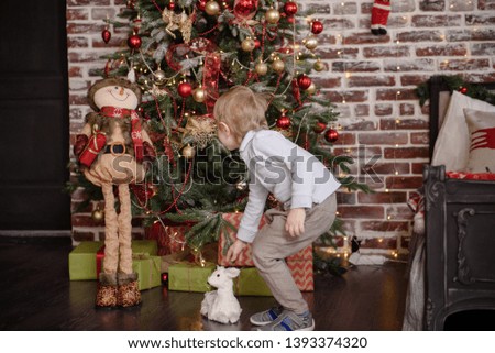 Happy cheerful little boy excited at Christmas Eve, sitting under decorated illuminated Christmas Tree. Greeting card or cover, horizontal with copy space.