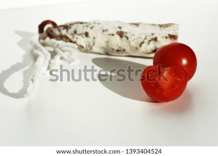 Traditional Spanish Fuet thin dried sausage with cherry tomatoes on white background